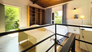 Ein Schlafzimmer mit einem Bett, Holzboden, einem Fenster mit Vorhängen und einem Nachttisch mit Lampe.