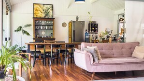 Ein großzügiger Wohnbereich mit Holzboden, einem rosa Sofa, einem Esstisch mit Stühlen und einer Küche im Hintergrund.