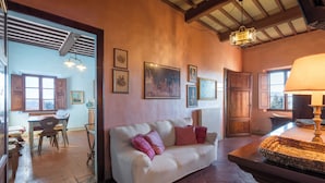 Una sala de estar acogedora con un sofá blanco, una mesa de madera con una cesta tejida, y un comedor con sillas y mesa de madera.