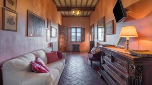 Una habitación acogedora con piso de madera, un sofá blanco con almohadas rosas, un armario de madera y un televisor colgado en la pared.