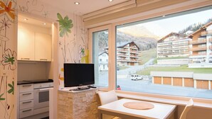 A modern kitchen with a stone backsplash, a flat-screen TV, and a dining area with a view of a mountain and buildings. - The Cristal apartment house is situated in a quiet, sunny and central location (Leukerbad)