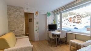 A hotel room with a stone wall, a desk with a computer, a bed, and a window with a view of a ski resort. - The Cristal apartment house is situated in a quiet, sunny and central location (Leukerbad)