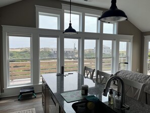 A kitchen with large windows, a granite countertop, and a view of the beach.