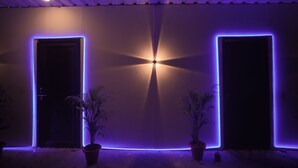 A building entrance with two doors, each framed by purple LED lights, and two potted plants on either side. - The Mahakumbh Vatika (Karchana)
