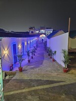 A corridor with potted plants and illuminated doors, leading to a building with a sign.