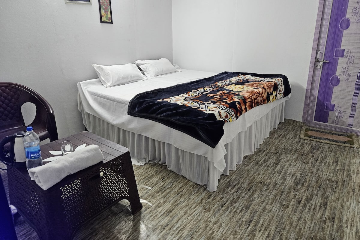 A small, neatly arranged bedroom with a bed, a chair, a table, and a door.