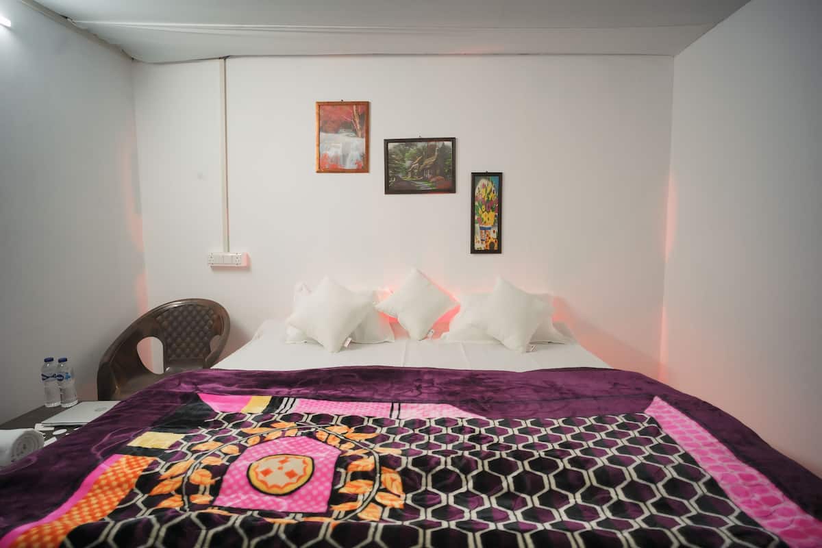 A neatly made bed with a patterned blanket, a chair, and a small table with a water bottle.