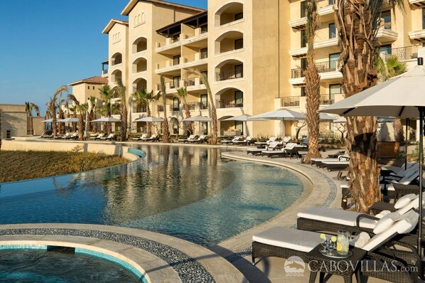 A hotel with a large pool, lounge chairs, and palm trees.