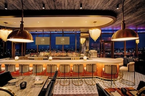 A bar area with a round bar, multiple seating arrangements, and pendant lighting. - Wind Creek Chicago Southland Casino and Hotel (Hazel Crest)