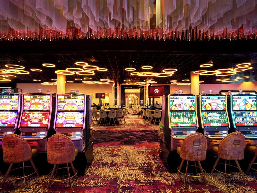 Um casino com várias máquinas de slot, piso coberto de carpete e um candelabro.