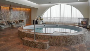 A modern indoor swimming pool with a tiled edge, a seating area with chairs, and a large window providing a view. - Wind Creek Southland Casino and Hotel (Hazel Crest)