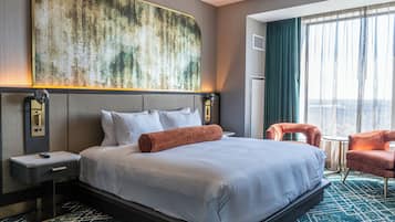 Une chambre d’hôtel avec un grand lit, une tête de lit agrémentée d’un décor mural texturé, une table de chevet, un bureau, deux chaises et une grande fenêtre avec des rideaux.