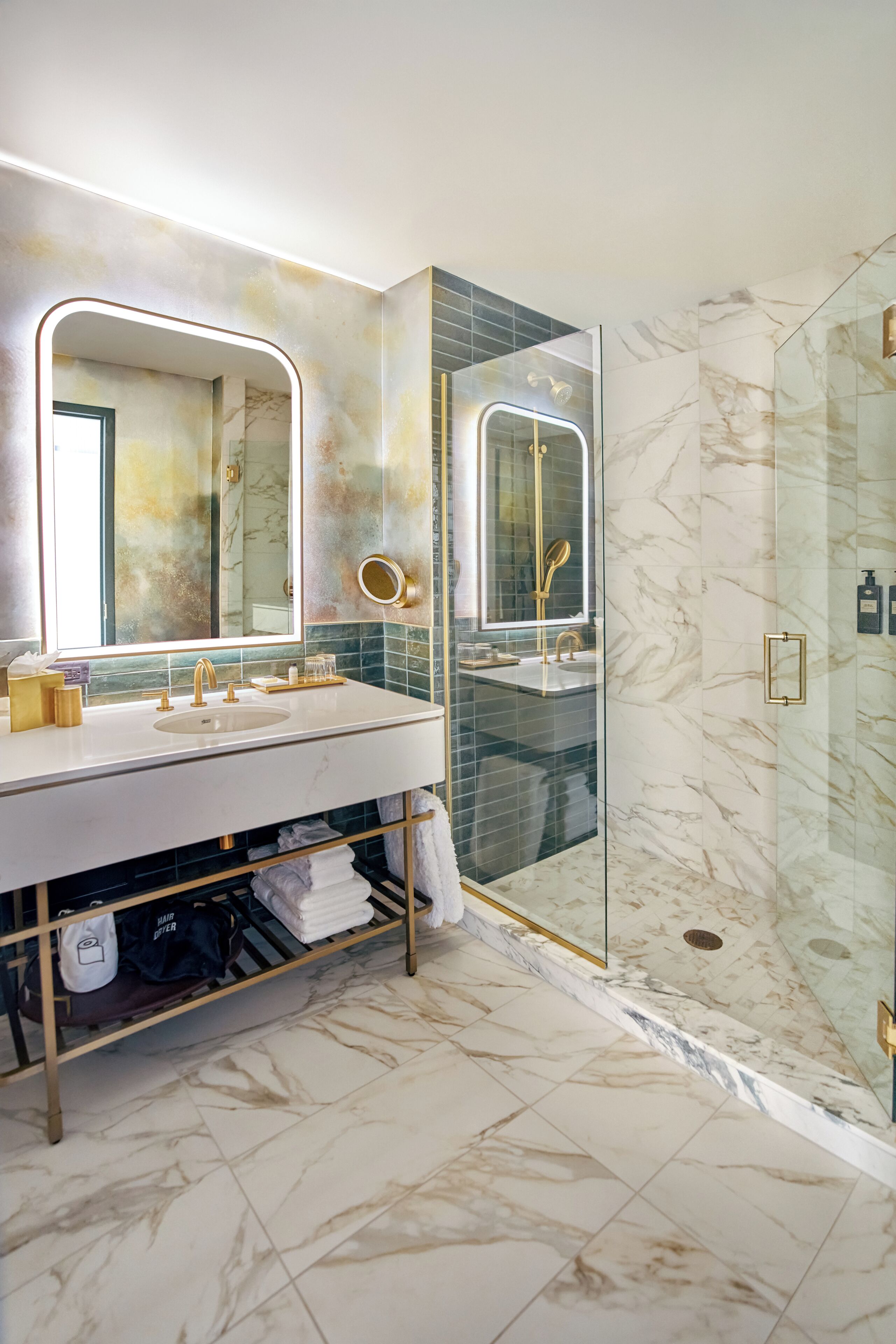 Un baño moderno con ducha de vidrio, suelo de mármol y tocador con espejo e iluminación.