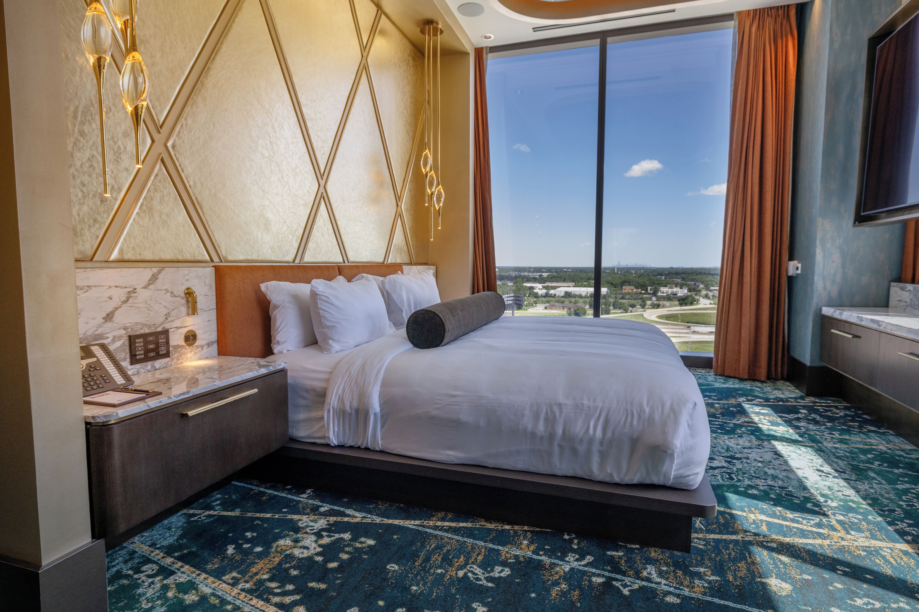A hotel room with a large bed, a nightstand, a telephone, and a view of the city.