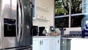 Ett modernt kök med ett kylskåp i rostfritt stål, vita skåp, en kaffebryggare och en vattenautomat.