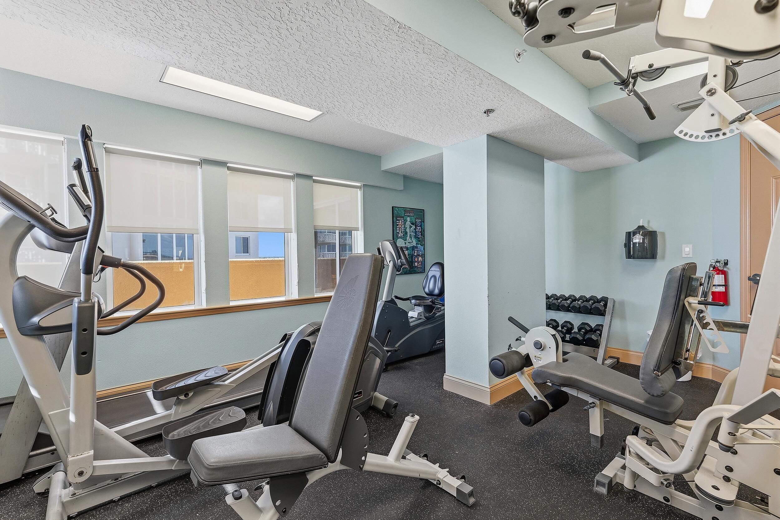 Une salle de sport équipée de matériel d’exercice, d’un téléviseur fixé au mur et d’une fenêtre avec des stores.