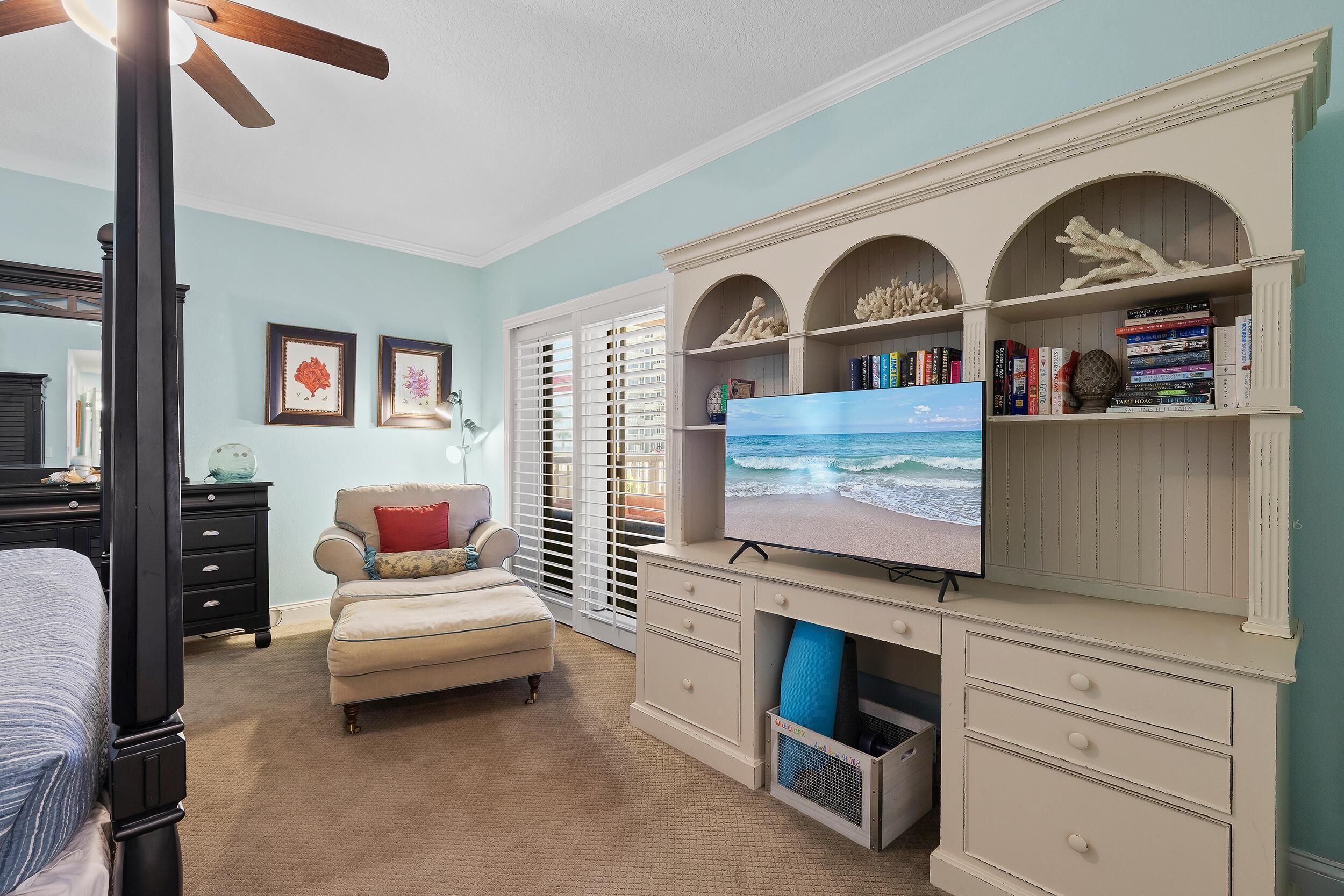 Un dormitorio con cama, escritorio con televisor, una silla y estantería.