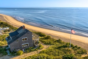 Una propiedad frente a la playa con una casa, una bandera y vista al océano.