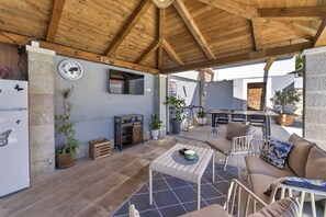 A covered outdoor patio with a wooden ceiling, a refrigerator, a table with chairs, and potted plants. - Nedia Retreat - Private Pool & Stunning Sea View (Mlini)