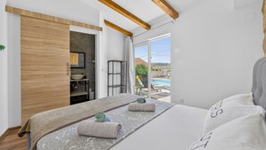 A bedroom with a large bed, wooden beams, a bathroom, and a view of a swimming pool. - Nedia Retreat - Private Pool & Stunning Sea View (Mlini)