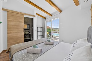 Un dormitorio con una cama grande, vigas de madera, un baño y vista a una piscina.