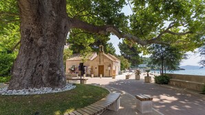 A coastal walkway with benches, a large tree, and a building with a bell tower. - Nedia Retreat - Private Pool & Stunning Sea View (Mlini)