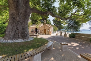 A coastal walkway with benches, a large tree, and a building with a bell tower. - Nedia Retreat - Private Pool & Stunning Sea View (Mlini)