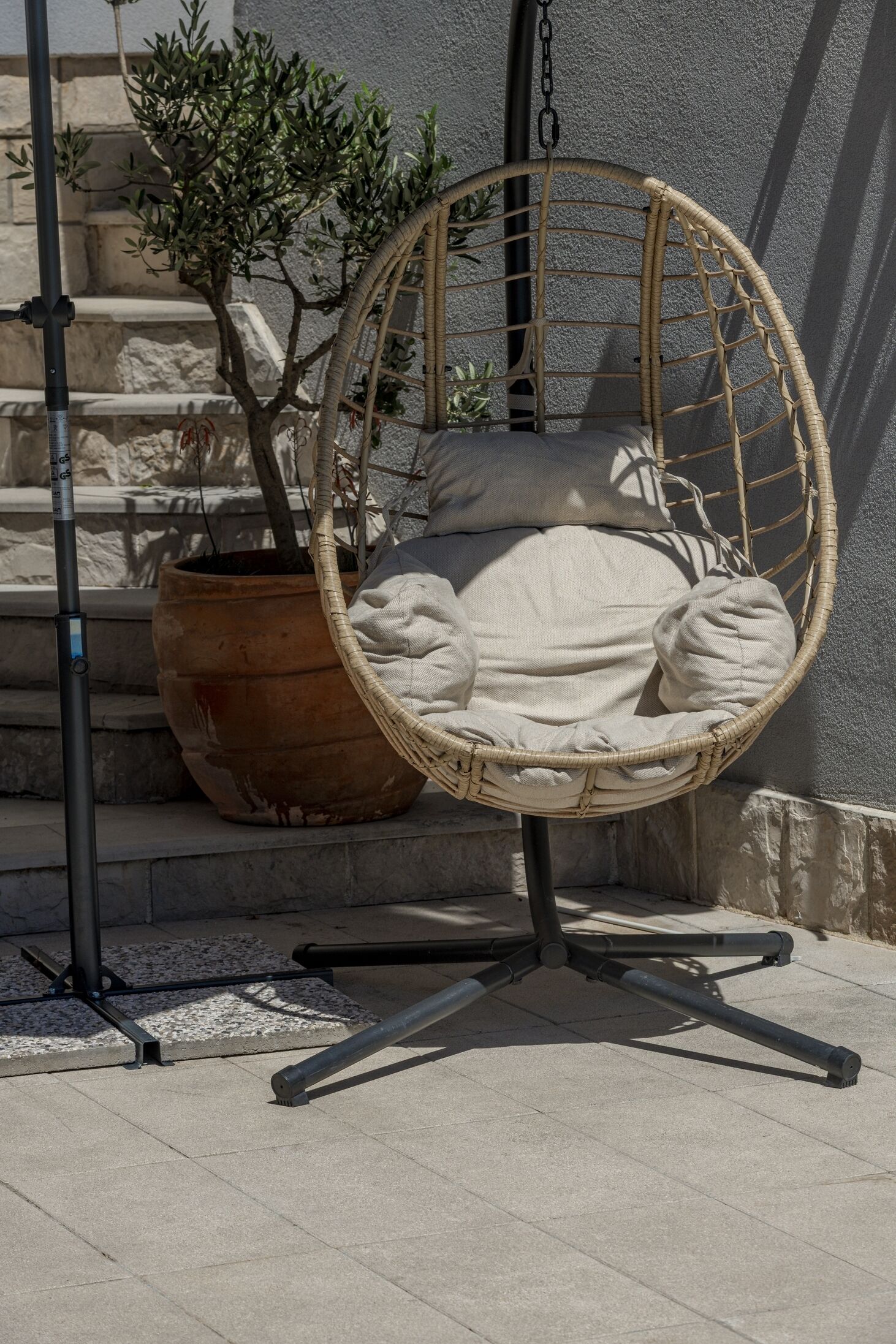 A wicker hanging chair with cushions, a potted plant, and a metal stand.
