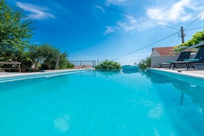 Ein klarer, blauer Pool mit Liegestühlen und einer Pergola auf der einen Seite.