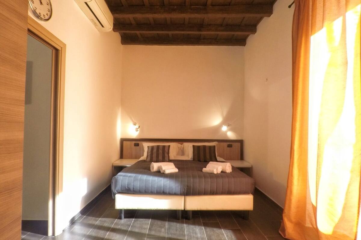 Quarto com cama, duas mesas de cabeceira, relógio e ar condicionado.