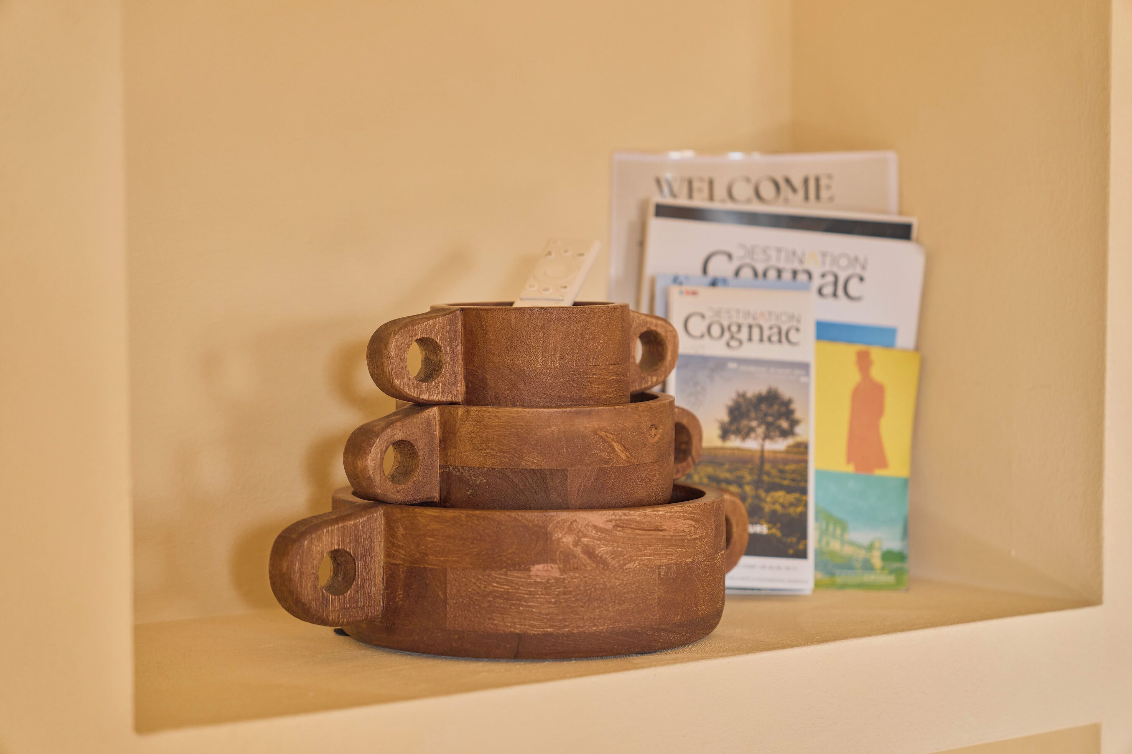 Una pila de tazas de madera sobre un estante con libros al fondo.