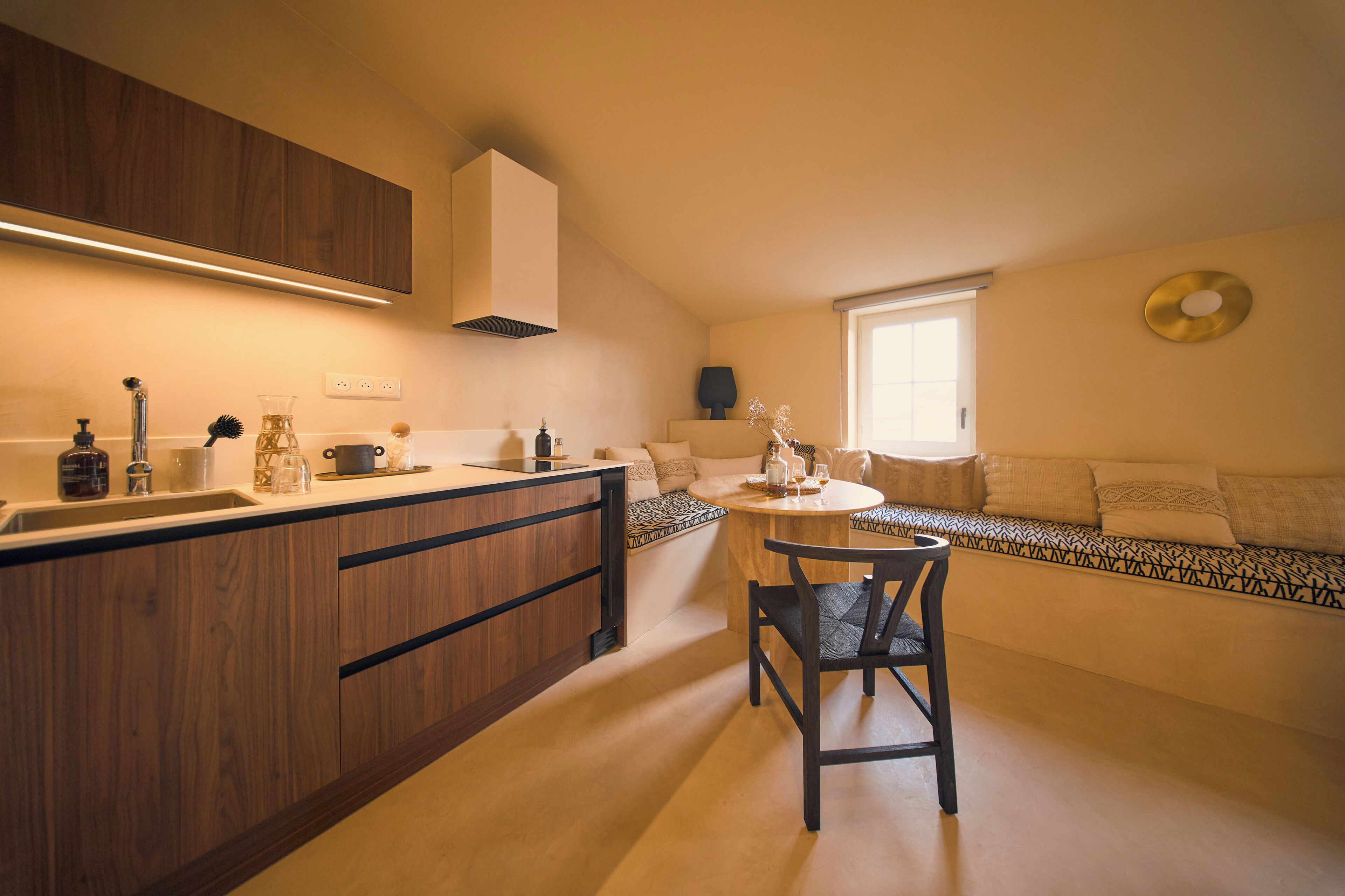 Une cuisine moderne avec des meubles en bois, un coin repas avec une table ronde et des chaises, et un banc intégré avec des coussins.