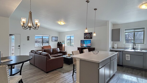 A modern kitchen with a central island, a dining area with a brown leather sofa, and a living room with a television. - BarknBike Abode Pets Bikes Desk Garage (Fruita)