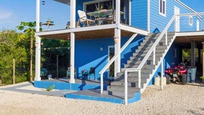 Una casa de dos pisos con balcón, escaleras y un área de estar cubierta al aire libre.