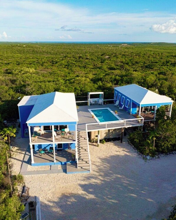 A two-story beachfront property with a swimming pool, outdoor seating, and a covered patio area.