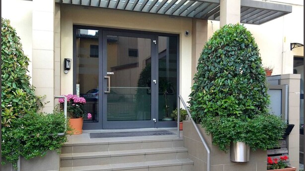 A modern building entrance with a glass door, a metal staircase, and potted plants. - 07. Apartment (Signa)