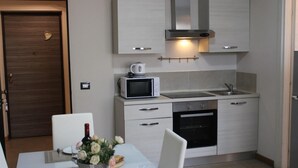 A modern kitchen with a microwave, oven, and sink. There is a dining table with chairs and a vase of flowers. - 07. Apartment (Signa)