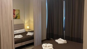 A hotel room with a bed, a wardrobe with a mirror, a bedside table with a lamp, and a window with curtains. - 07. Apartment (Signa)