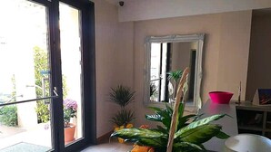 A room with a sliding glass door leading to a balcony, a large mirror on the wall, and a potted plant in the center. - 07. Apartment (Signa)
