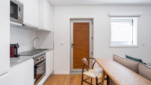 A compact kitchen with a microwave, stove, and sink. A wooden door leads to a dining area with a table and a chair. - GuestReady - Restful Getaway in Matosinhos (Matosinhos)