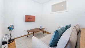 A modern living room with a sofa, a coffee table, a TV, and a standing fan. - GuestReady - Restful Getaway in Matosinhos (Matosinhos)