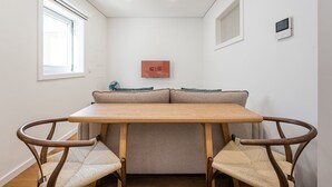 A small, modern room with a wooden table and two wicker chairs, a sofa with cushions, a window, and a wall-mounted device. - GuestReady - Restful Getaway in Matosinhos (Matosinhos)