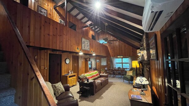 Ein geräumiges Loft mit hohen Decken, Holzbalken und einer Treppe. Es bietet einen gemütlichen Sitzbereich mit einer Couch, einem kleinen Tisch und einem Couchtisch. Es gibt einen Essbereich mit Tisch und Stühlen, und ein großes Fenster, das für natürliches Licht sorgt.