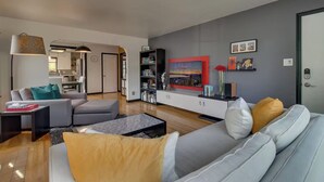 A modern living room with a grey sofa, a coffee table, and a bookshelf. There is a dining area visible in the background. - NEW Old Southwest Gem, Patio, Grill, Smart TV, 2 Desks + Fitness Equipment

 (Reno)