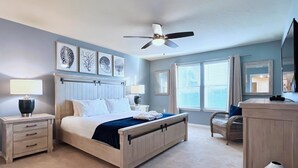 Un dormitorio con cama, mesitas de noche, ventilador de techo, obras de arte y una ventana con persianas.