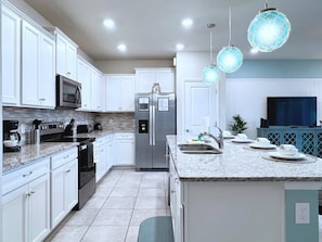 A modern kitchen with white cabinetry, stainless steel appliances, a granite countertop, and pendant lighting.