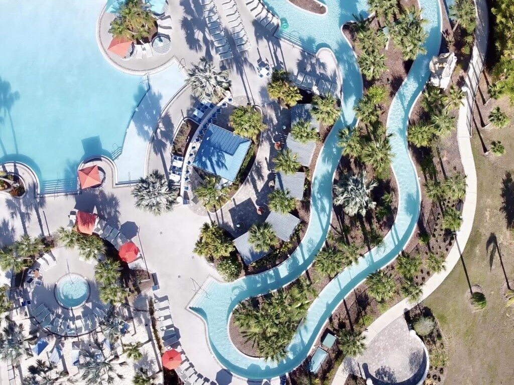 Ein Luftbild eines Resorts mit einem gewundenen Pool, Liegestühlen und Palmen.