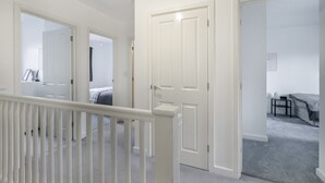 A hallway with white doors leading to bedrooms, a small table with a chair, and a light fixture on the ceiling.
