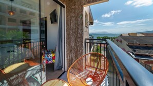 A balcony with a glass door, a red chair, and a view of the sea.