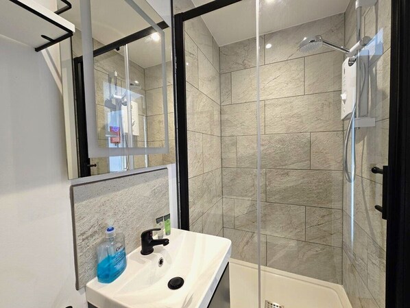 Une salle de bain moderne avec une douche à parois de verre, un lavabo blanc avec un miroir et un flacon de savon liquide bleu.